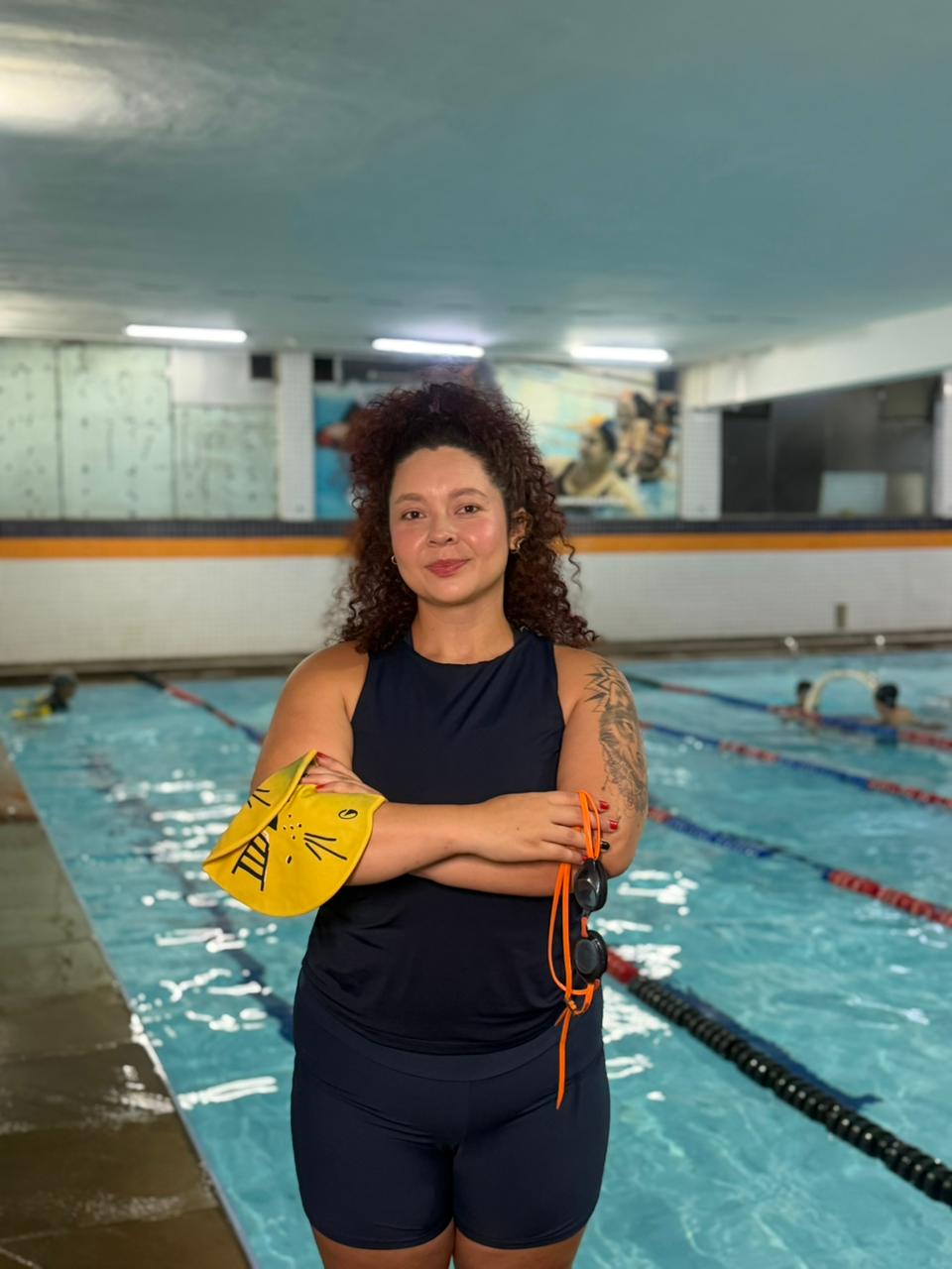 Carina Maria sorrindo de braços cruzados em frente à piscina